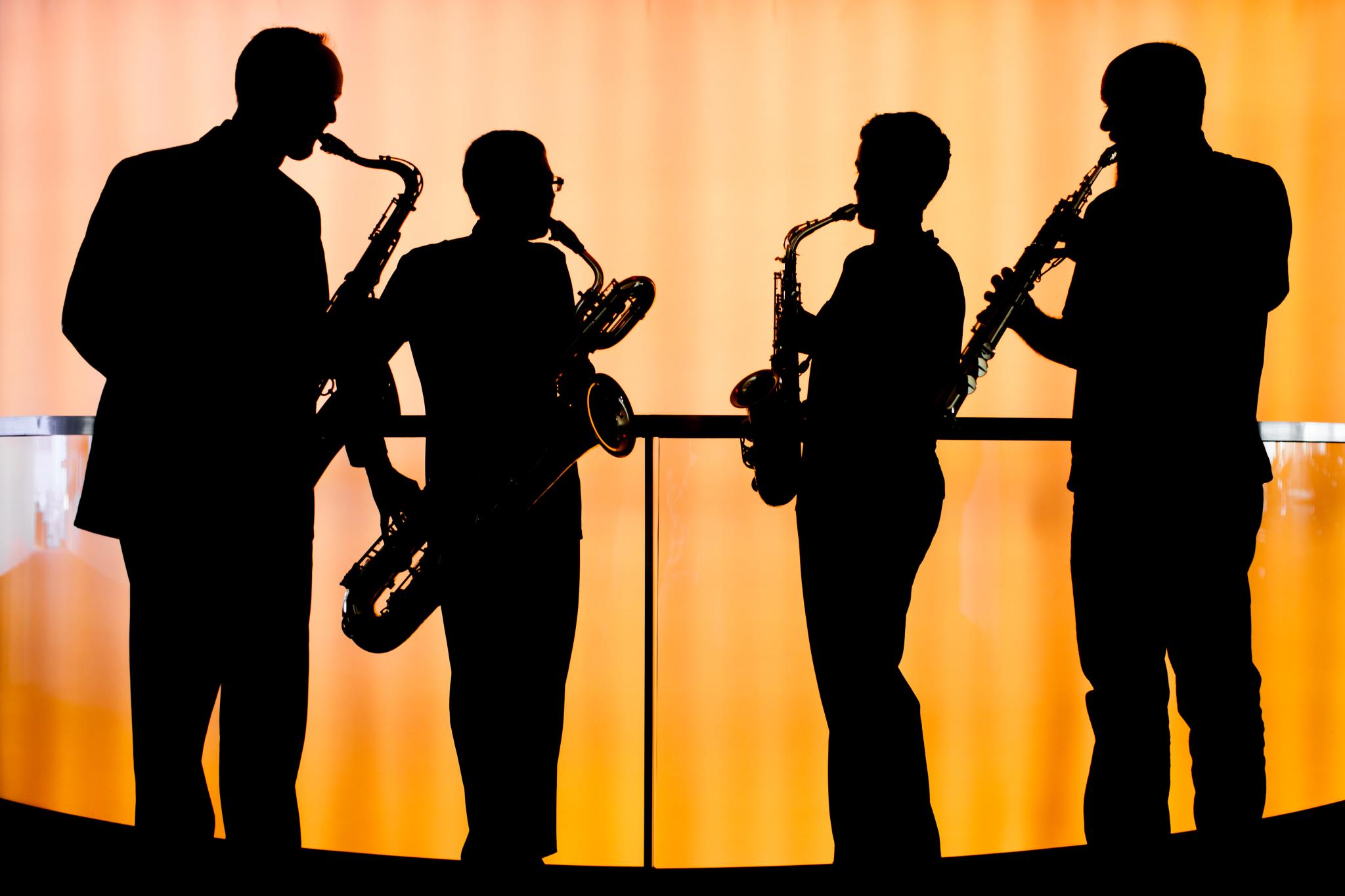 four people silhouetted against orange background playing saxaphones