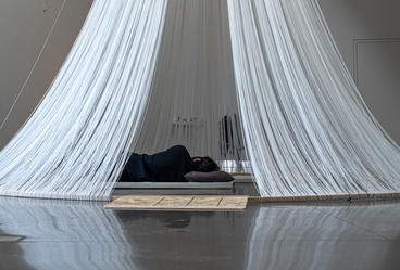 person lays down surrounded by artpiece made of string/yarn