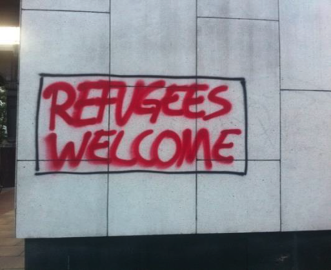 Red spraypaint on a cinderblock wall reading "Refugees welcome"