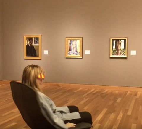 a person sitting in a chair by 3 paintings on a wall