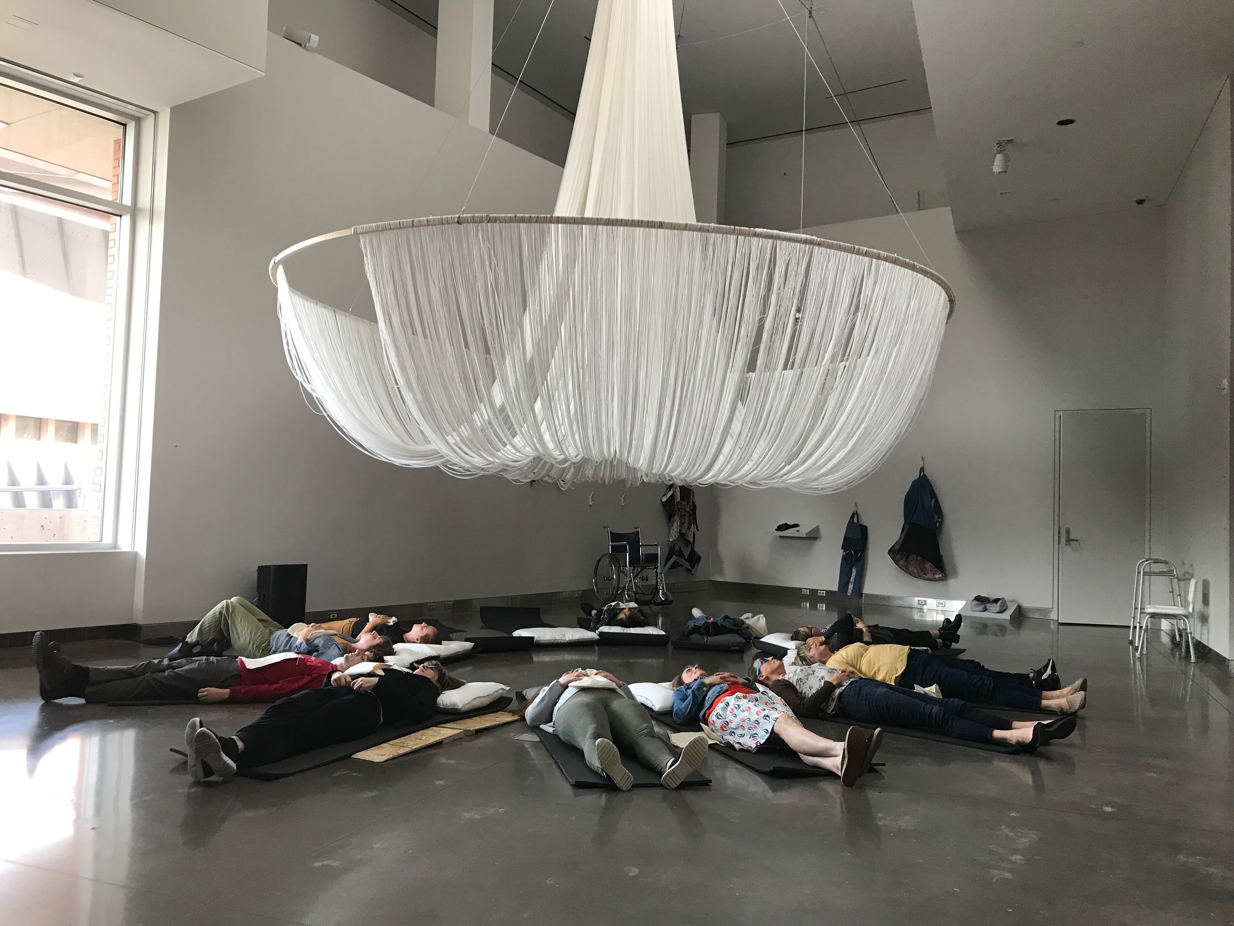 People laying in a circle underneath a string art piece