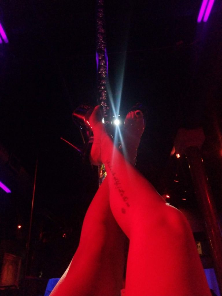 A photo from the perspective of a dancer with bare legs and large platform heels, hanging upside-down by their legs from a pole.