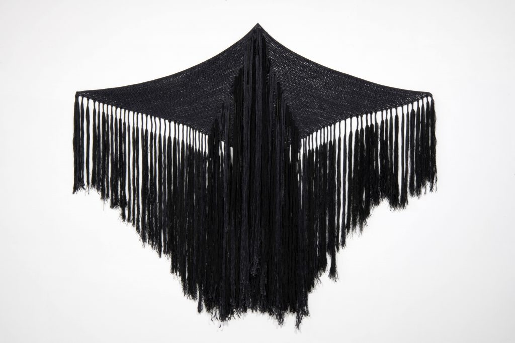 A black, diamond-shaped textile with fringe across the middle and bottom hangs open. 