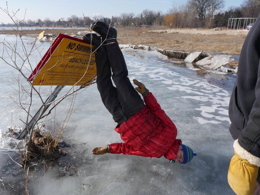 A person with their feet up on a sign and their face resting on a frozen lake