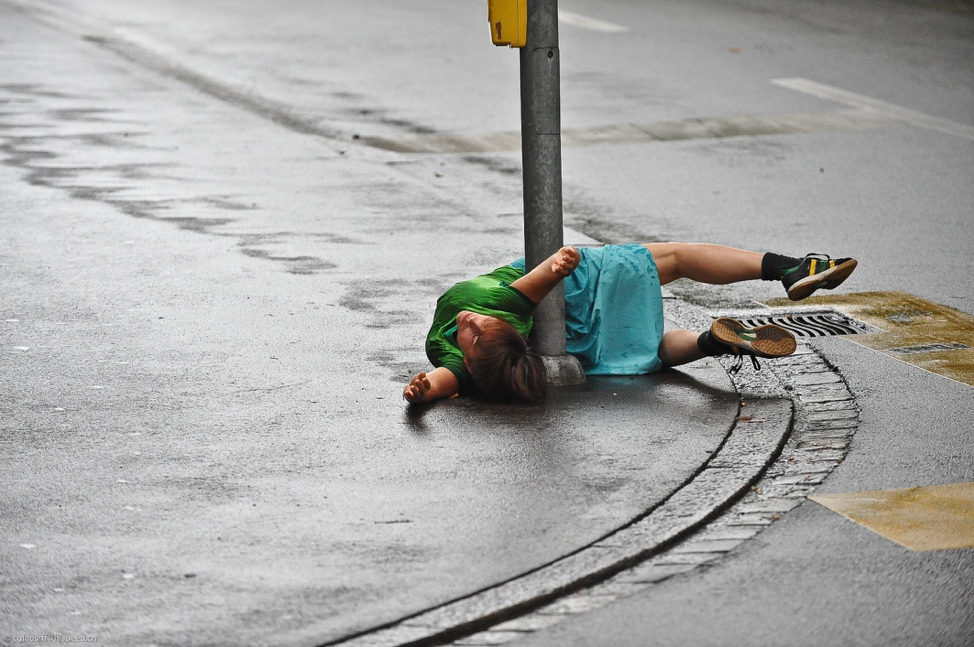 A person lying on the street grasping a signpost