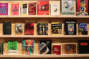 A display of book covers on a wooden shelf representing a selection of disapproved books; titles include "Grant Writing for Dummies," "Trans Bodies, Trans Selves," and "No Disrespect" by Sister Souljah