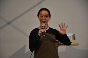 Artist Yuko Taniguchi speaks into a microphone during the "Pieces We Hold" workshop.
