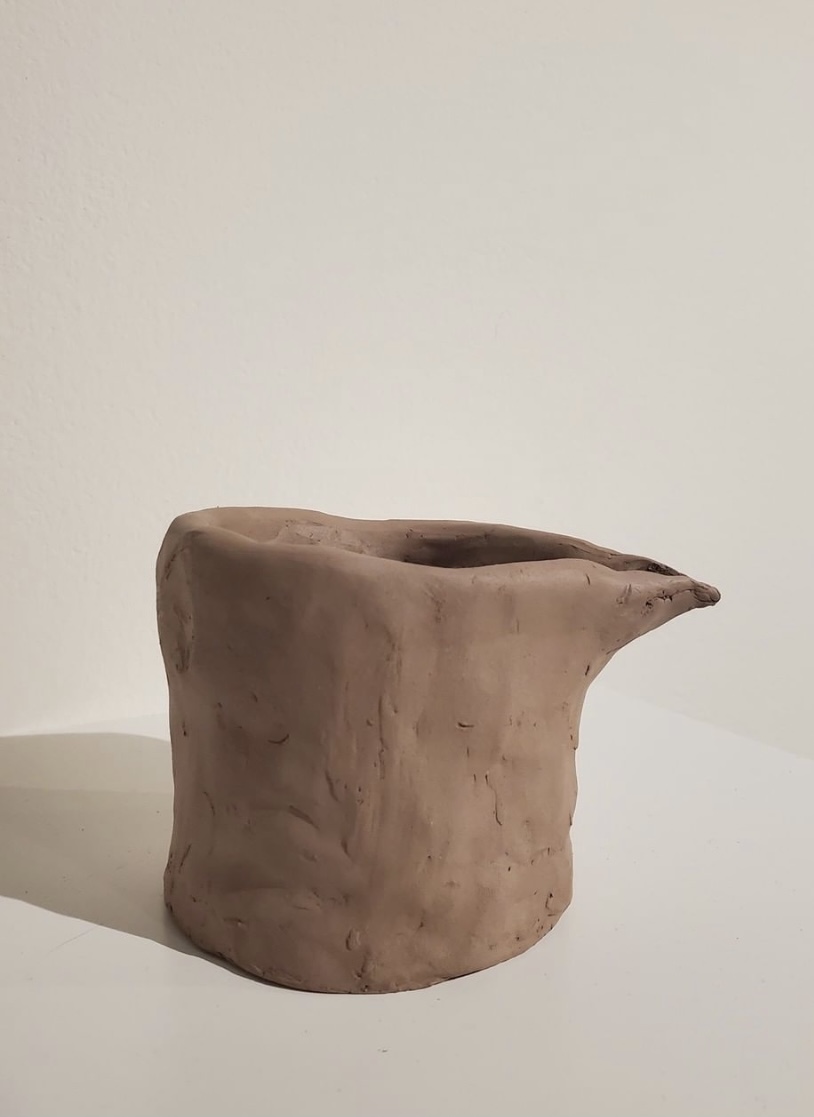 Raw clay shaped into a rough creamer. Clear marks of fingertips pressing into the clay.