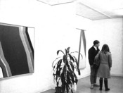 2 people beside a plant and some artwork on the wall