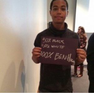 a person holding a sign saying '50% black, 50% white, 100% Ben Hugh'