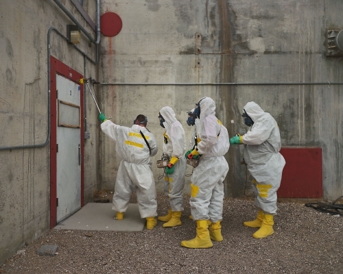 4 people in hazmat suits near a white door