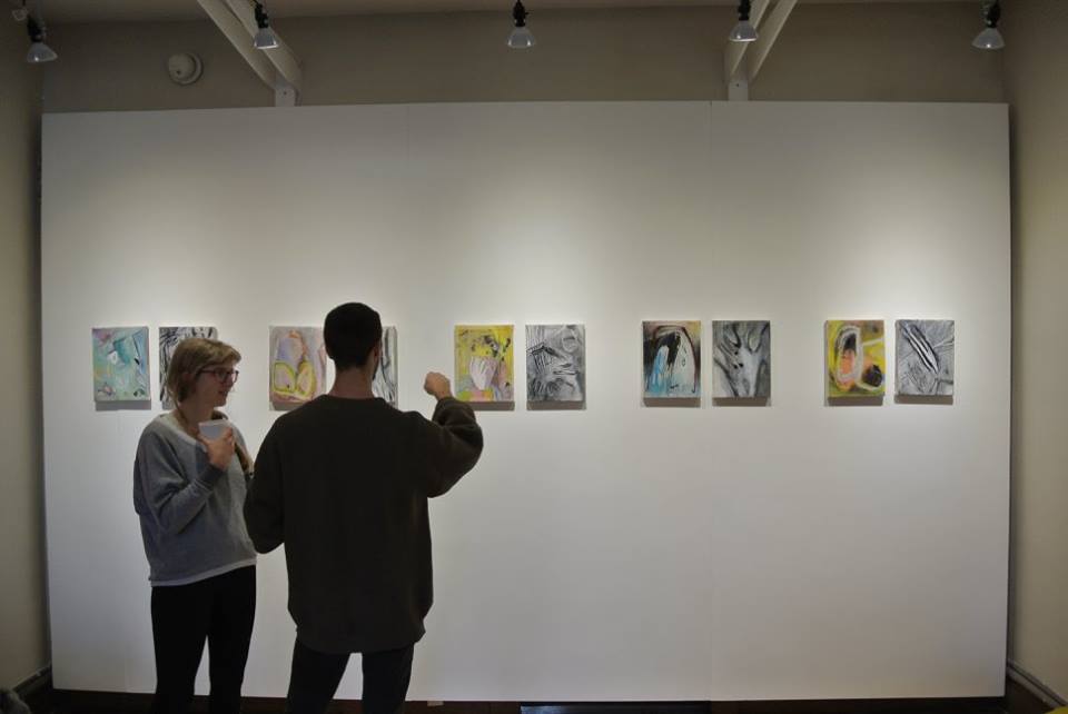 2 people looking at a row of paintings on a wall