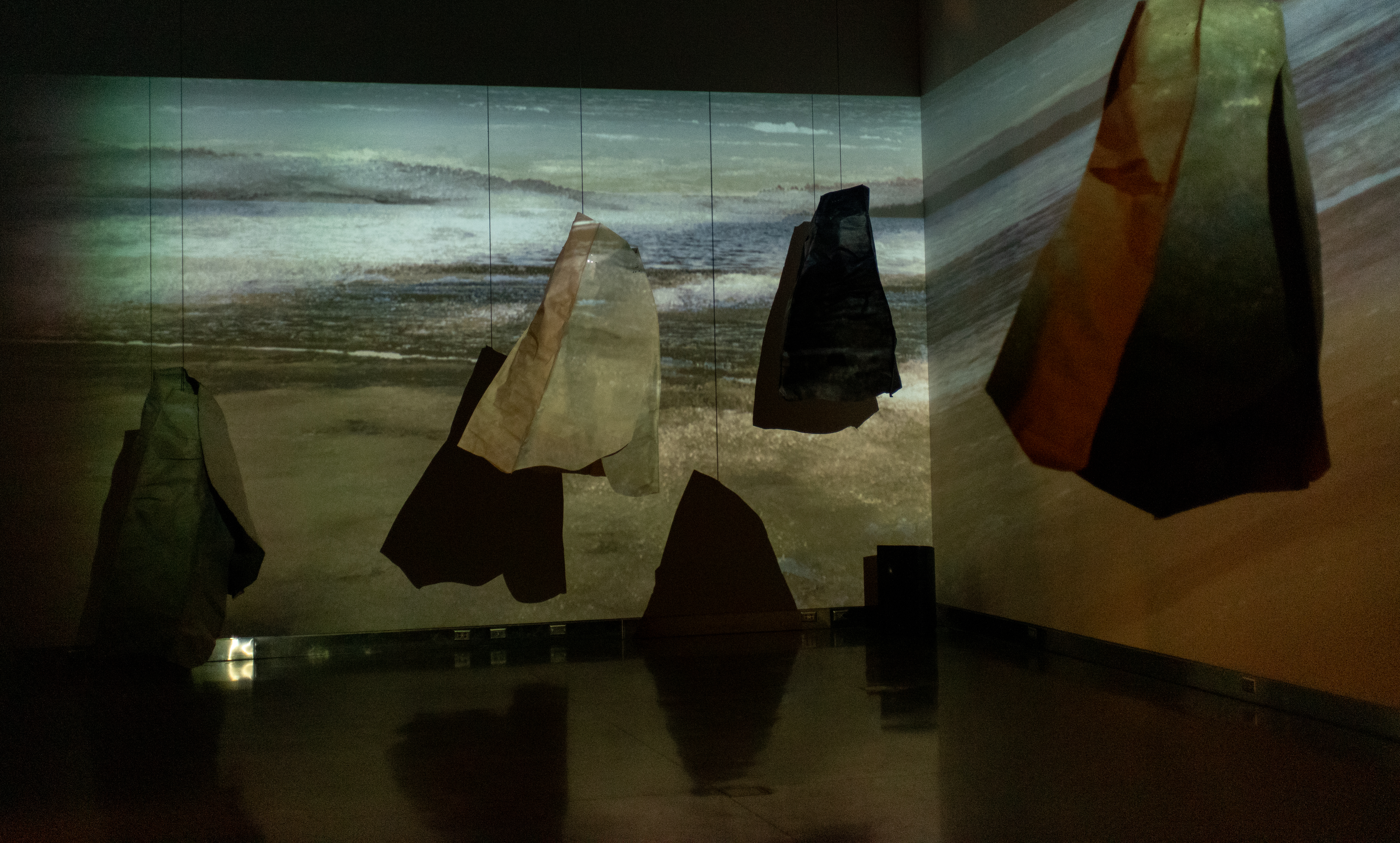 art installation with clothes hanging amid projection of sand and stormy sky