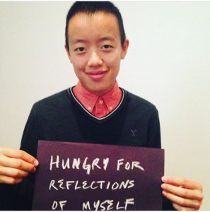A person holding a sign saying 'hungry for reflections of myself'