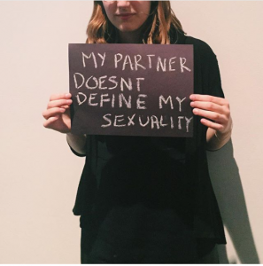 a person holding a sign saying 'my partner doesn't define my sexuality'