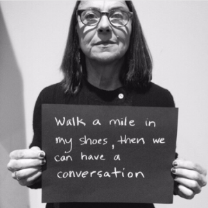 a person holding a sign saying 'walk a mile in my shoes, then we can have a conversation'