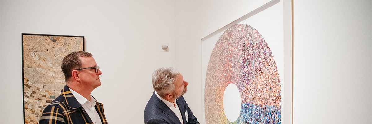 Two men look quizzically at a color wheel made from thousands of tiny images sourced from Google. 