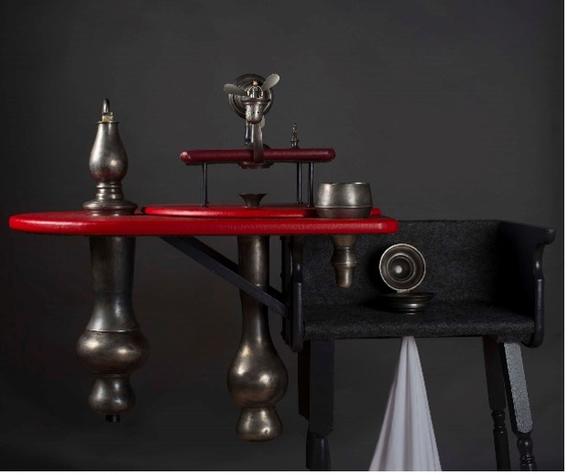 Pewter devices in the shape of teardrops atop a bright red shelf with other wooden and metal implements. The effect is that of a steampunk distillation device.