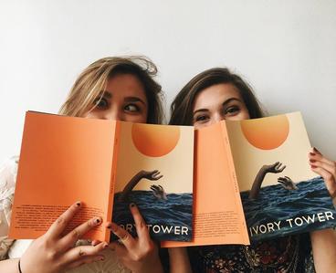two people holding up Ivory Tower booklets over faces