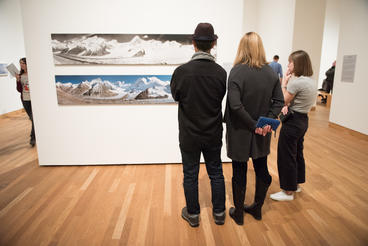 three people viewing landscape art on wall