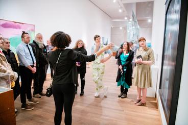 A person gesturing a group of people towards an art piece