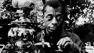 A Black male looks solemnly off camera while dispensing water from a silver carafe (black and white image).