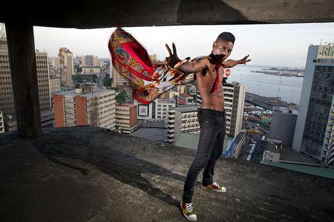 A person shirtless wearing a cape, surrounded by buildings