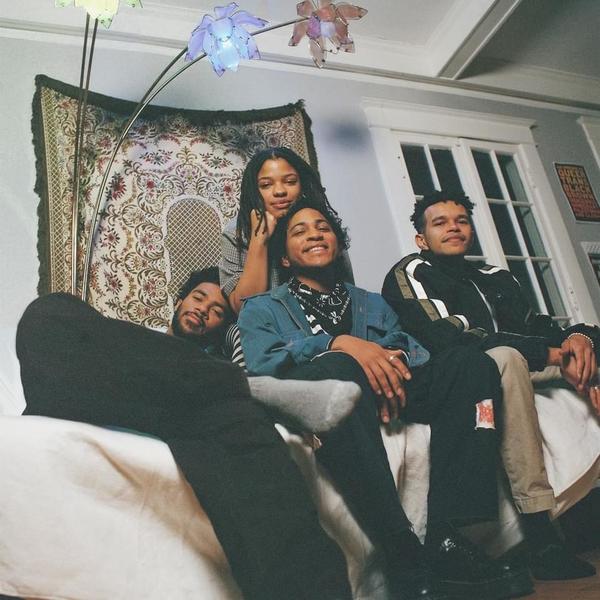 Band photo of musicians pictured in a living room, gathered around and on a couch